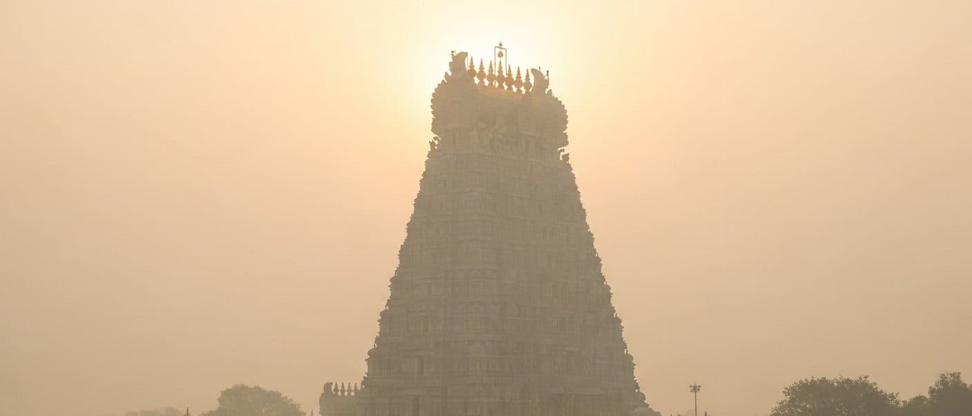 The gopuram of the Meenakshi Amman Temple in Madurai at dawn, seen through morning mist, gold detail catching first light